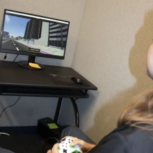 Picture of Josh sitting at computer with video game controller in his hand and mock city on the computer screen.