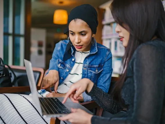 two women looking and pointing at macbook laptop